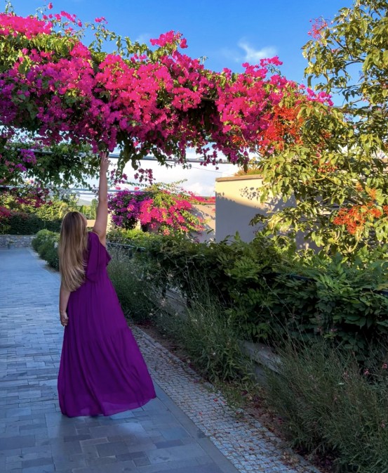 Joice in a long purple dress under pink bougainvillea