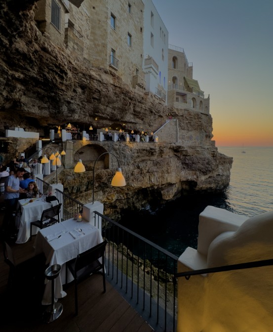 Restaurant tables set in a cave above the sea at sunset